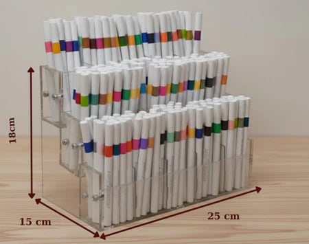 Kệ bút mica 3 tầng đầy bút, vách trước tầng dưới còn lộ rõ